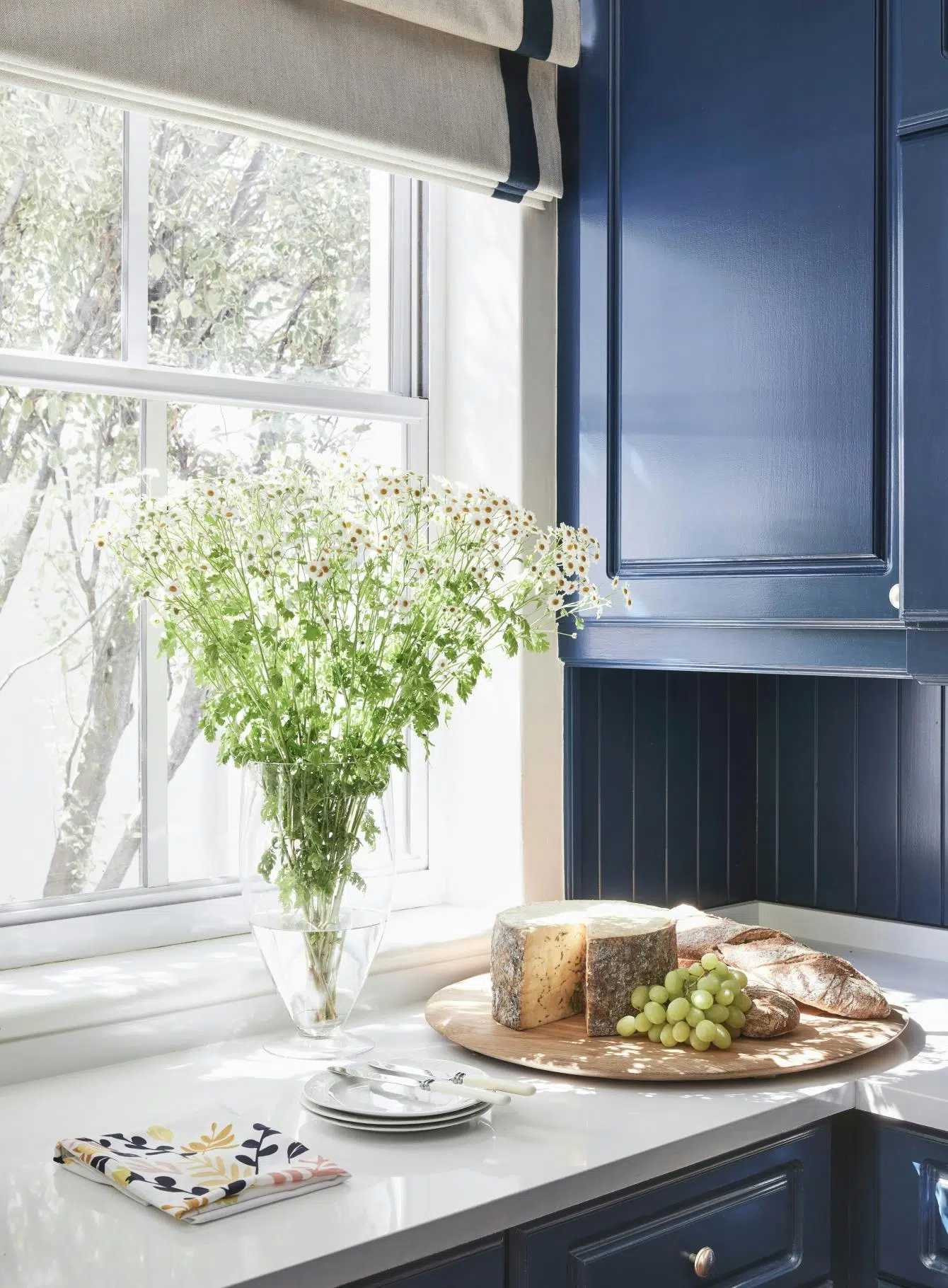 Close-up of a kitchen with dark blue cabinetry, a window with a view of the outdoors and a charcuterie board on the countertop.