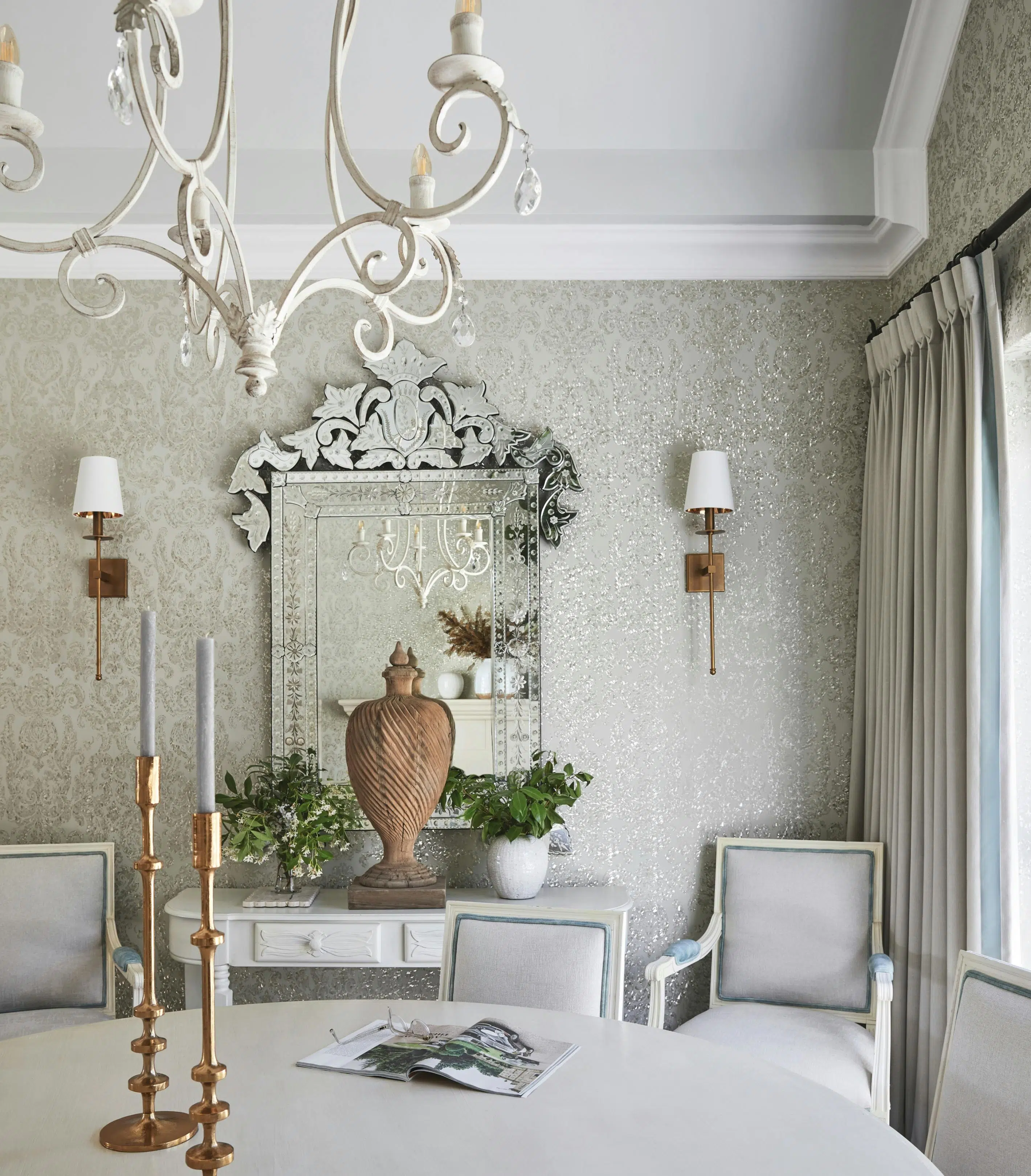 A French-style dining area with a chandelier at the top, a dining table with candelabras on top, with a mirror on the wall in the background.